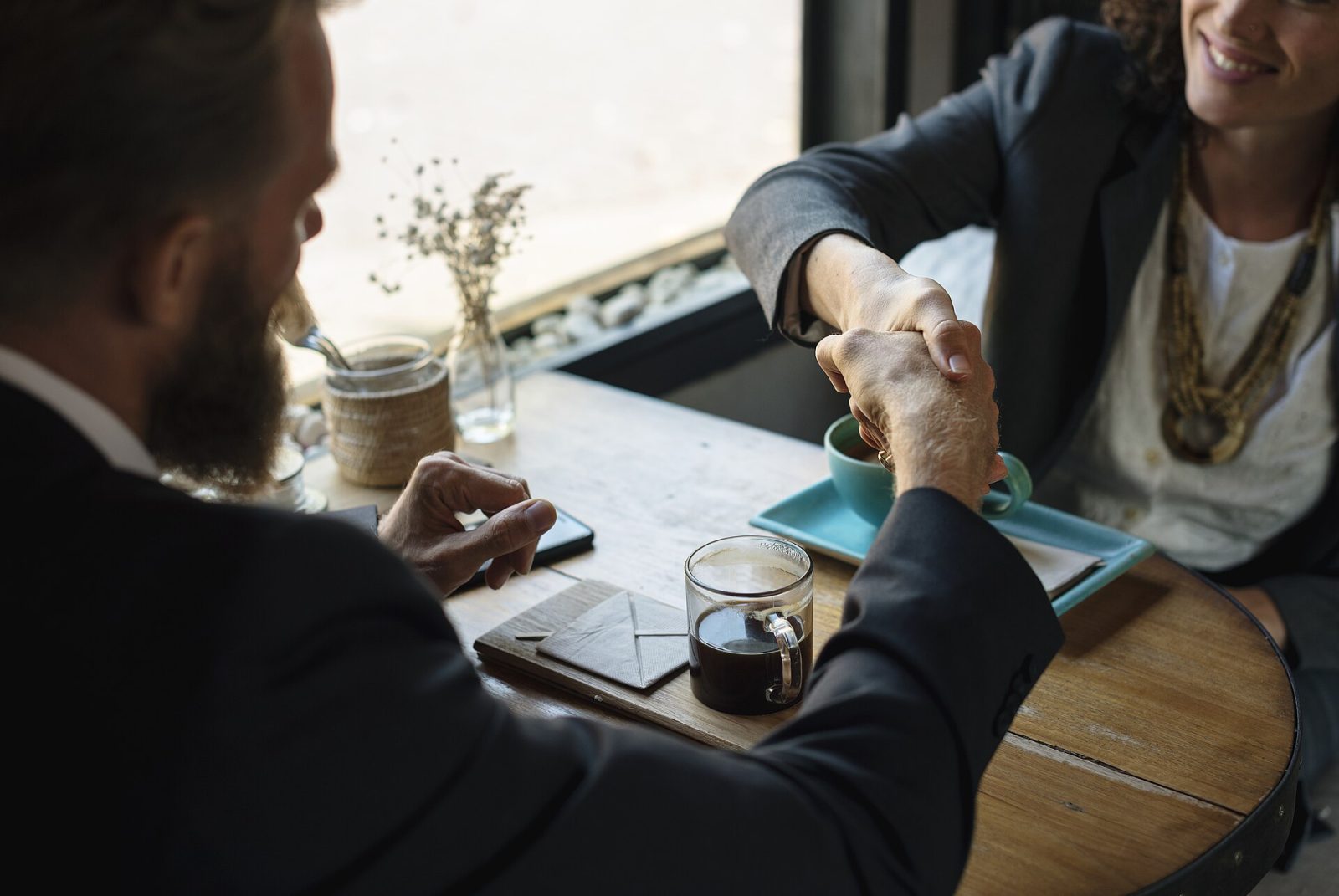 Two business professionals shaking hands over coffee after agreeing on a consulting engagement